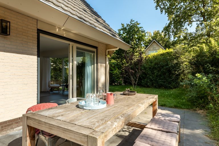 Zijtuin met eettafel vrijstaand vakantiehuis Veluwe zonnig terras